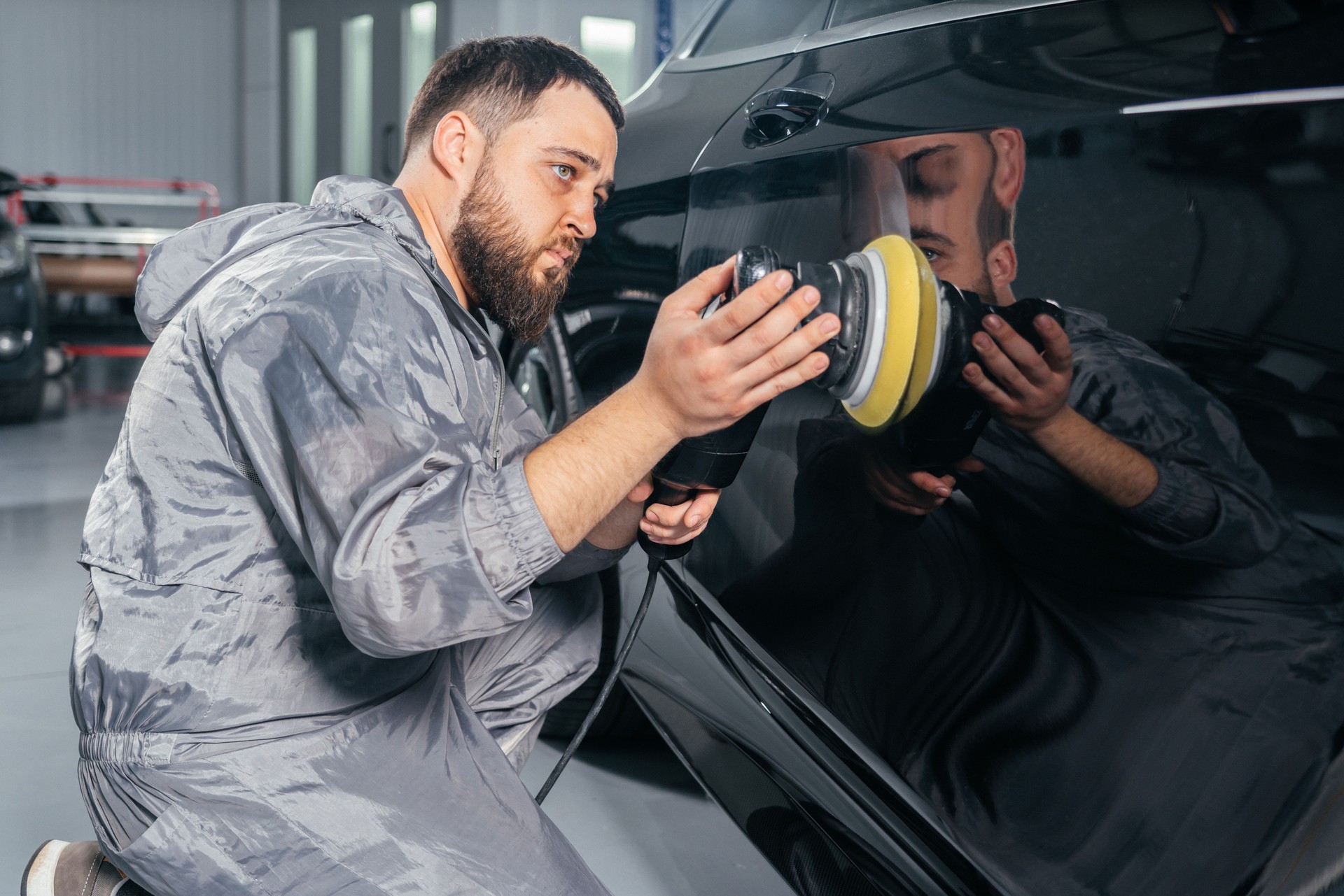 Worker polishing car with special grinder and wax from scratches at the car service station. Professional car detailing and maintenance concept