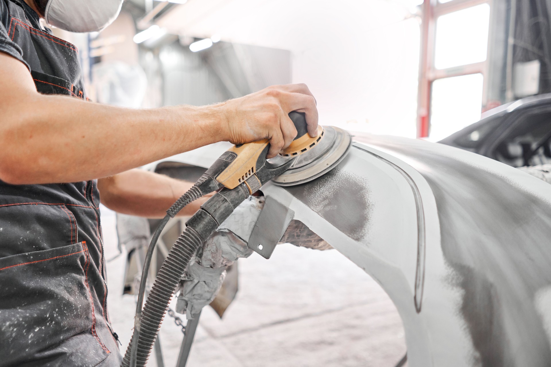 The mechanic works with a grinding tool. Sanding of car elements. Garage painting car service. Repairing car section after the accident.