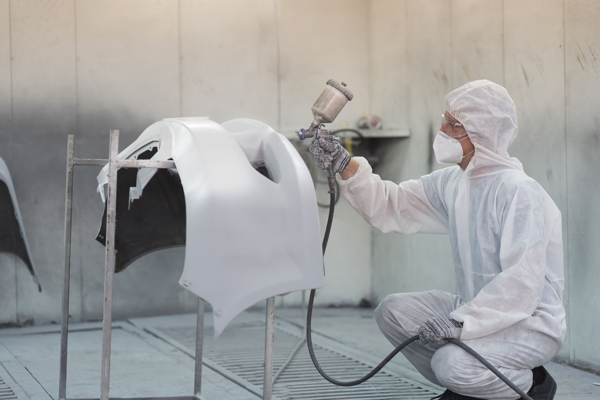 Automotive paint service. Quality auto body shop concept. Male car mechanic working with spray gun painting auto body in automotive paint service shop. Automobile painter painting car frame in chamber